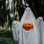 family dressed in ghost costumes posing in the woods with a pumpkin